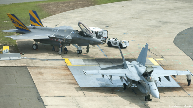 A Navy F-35C and the plane it will replace, the F/A-18E Super Hornet, sit together on a runway.