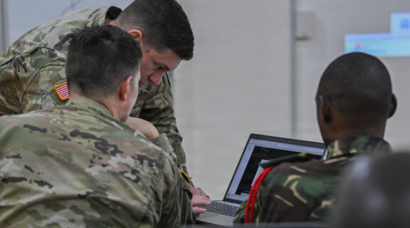 U.S. Army Chief Warrant Officer 2 Scott Lowry, senior host analyst, and Chief Warrant Officer 2 Benjamin Brown, cyber operations technician, with the 200th Cyber Protection Team, U.S. Army Cyber Protection Brigade, assist a member of the Tanzania People’s Defence Force while attending a course on defensive cyber operations during exercise Justified Accord 26, Dar Es Salaam, Tanzania, March 5, 2026. (U.S Air Force photo by Staff Sgt. Jan K. Valle)