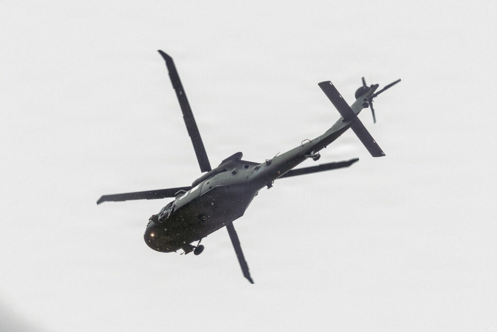 A UH-60 Black Hawk helicopter flies overhead as Soldiers assigned to the Military District of Washington prepare to board between events during the 2026 Best Squad Competition at Fort A.P. Hill, Virginia, May 7, 2026. The competition challenges Soldiers through a series of physically and mentally demanding events designed to assess tactical proficiency, teamwork and combat readiness. (U.S. Army photo by Sgt. Christopher Smith)