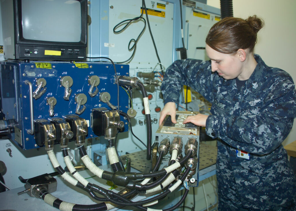 A Navy technician wrestles with an unwieldy mass of electronic cables.