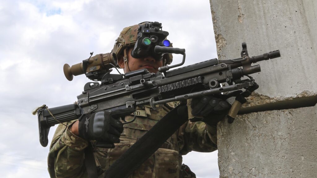 A soldier uses special binoculars to see through a weapon sight.