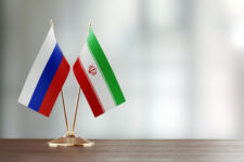 Russian And Iranian Flag Pair On A Desk Over Defocused Background