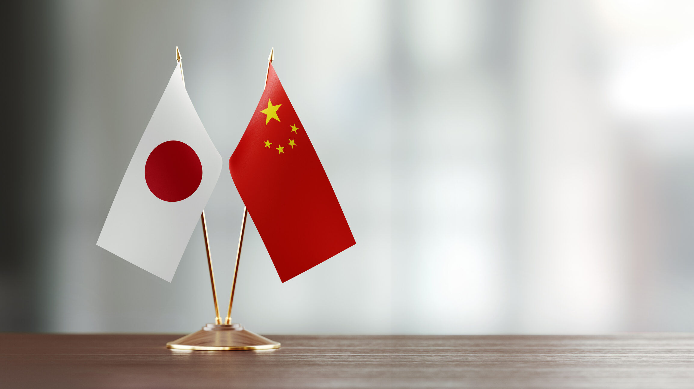 Japanese And Chinese Flag Pair On A Desk Over Defocused Background